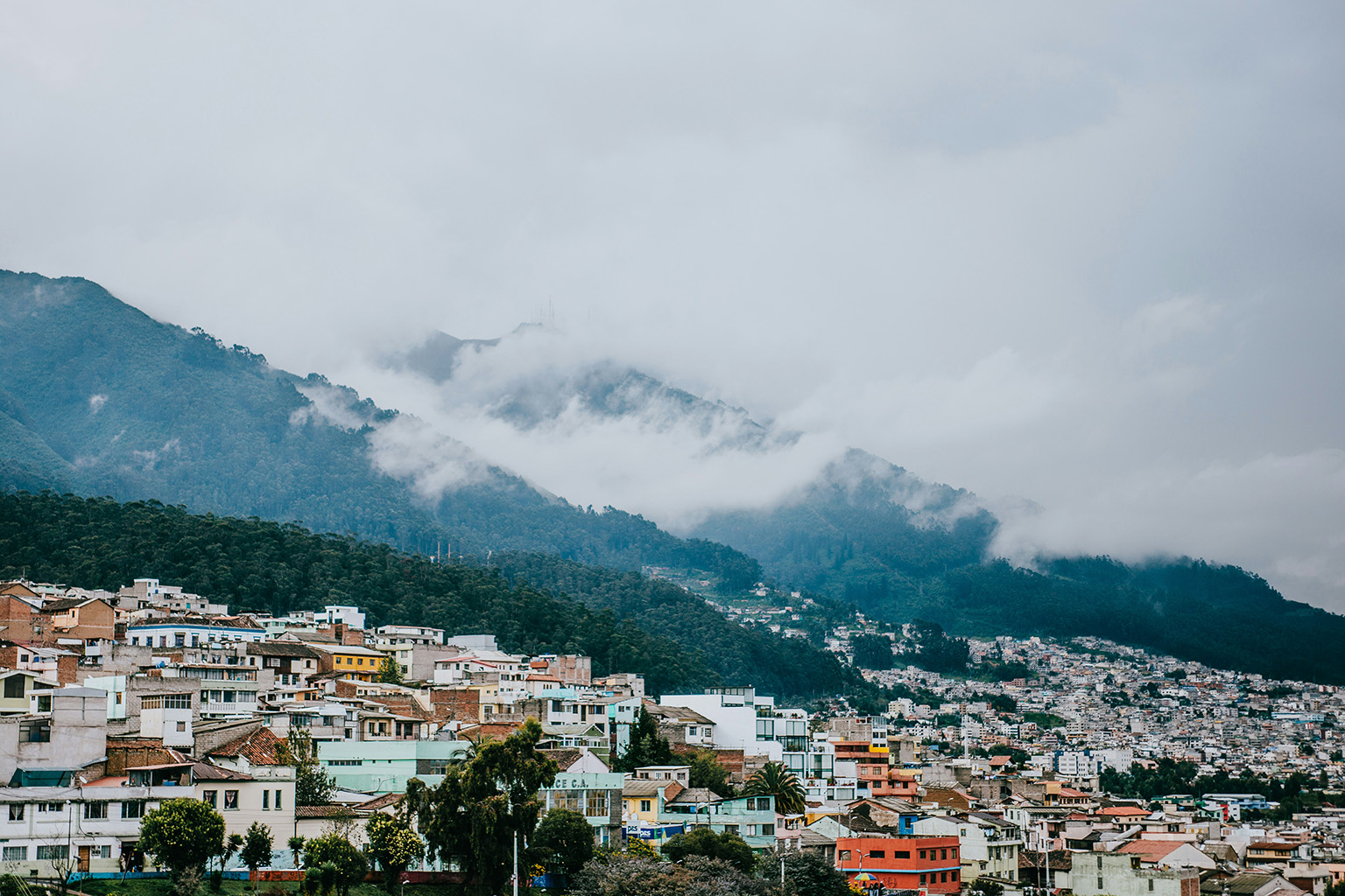 Clouds floating over the hills surrounding Quito, Ecuador, with the city visible below, showcasing the stunning landscape.