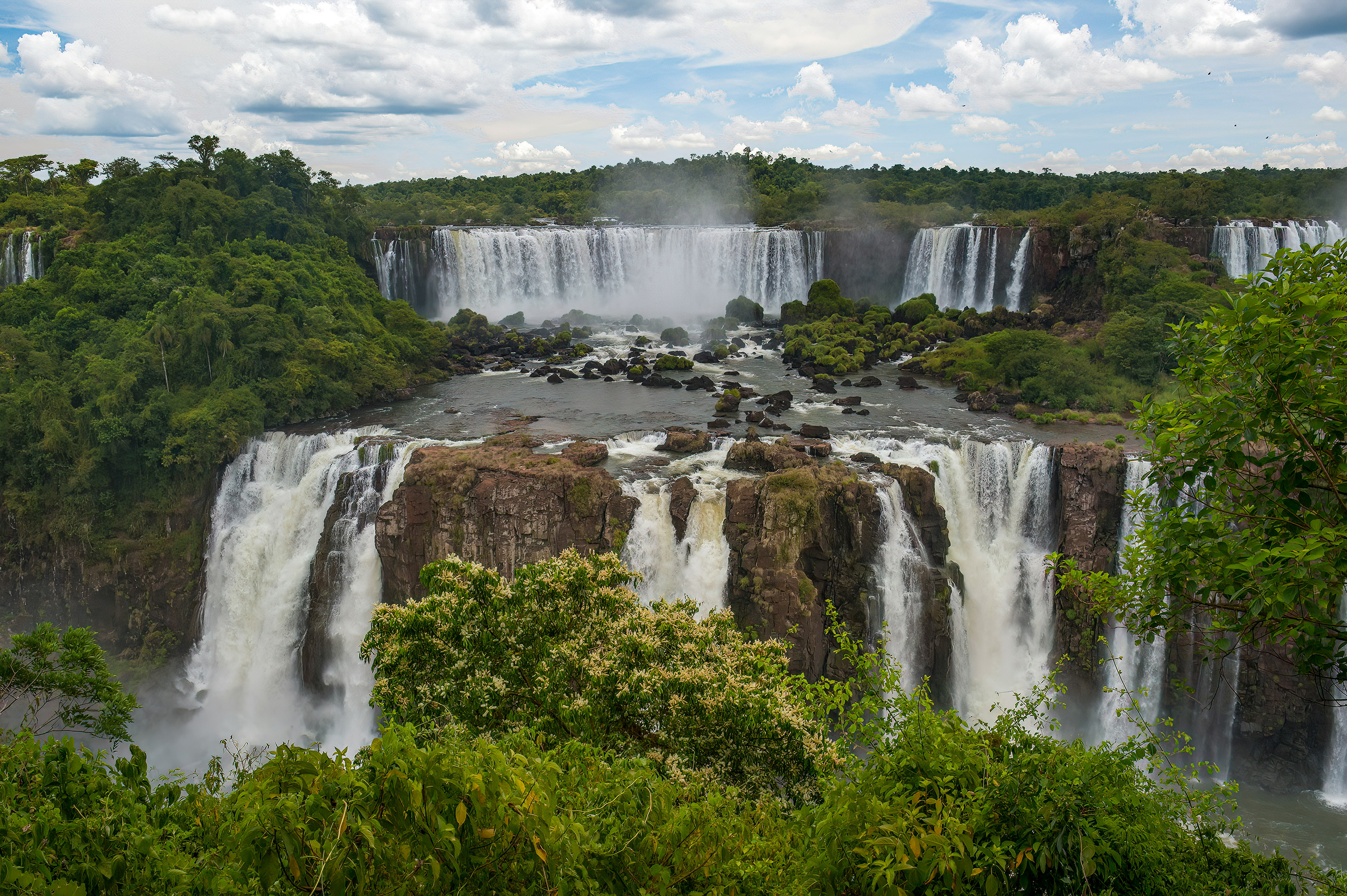 Panoramic shot of Iguazu Falls, showcasing the waterfalls and surrounding lush greenery in Latin America.