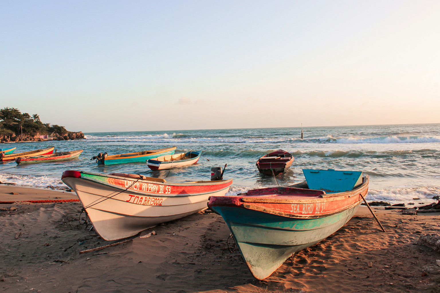 Wooden boats on a sandy tropical beach under a clear blue sky in the Caribbean.