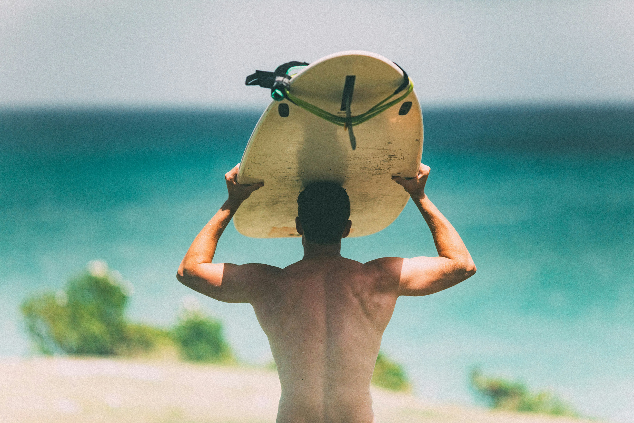 Muscular man holding a surfboard over his head while walking to the beach in the Caribbean, ready to surf.