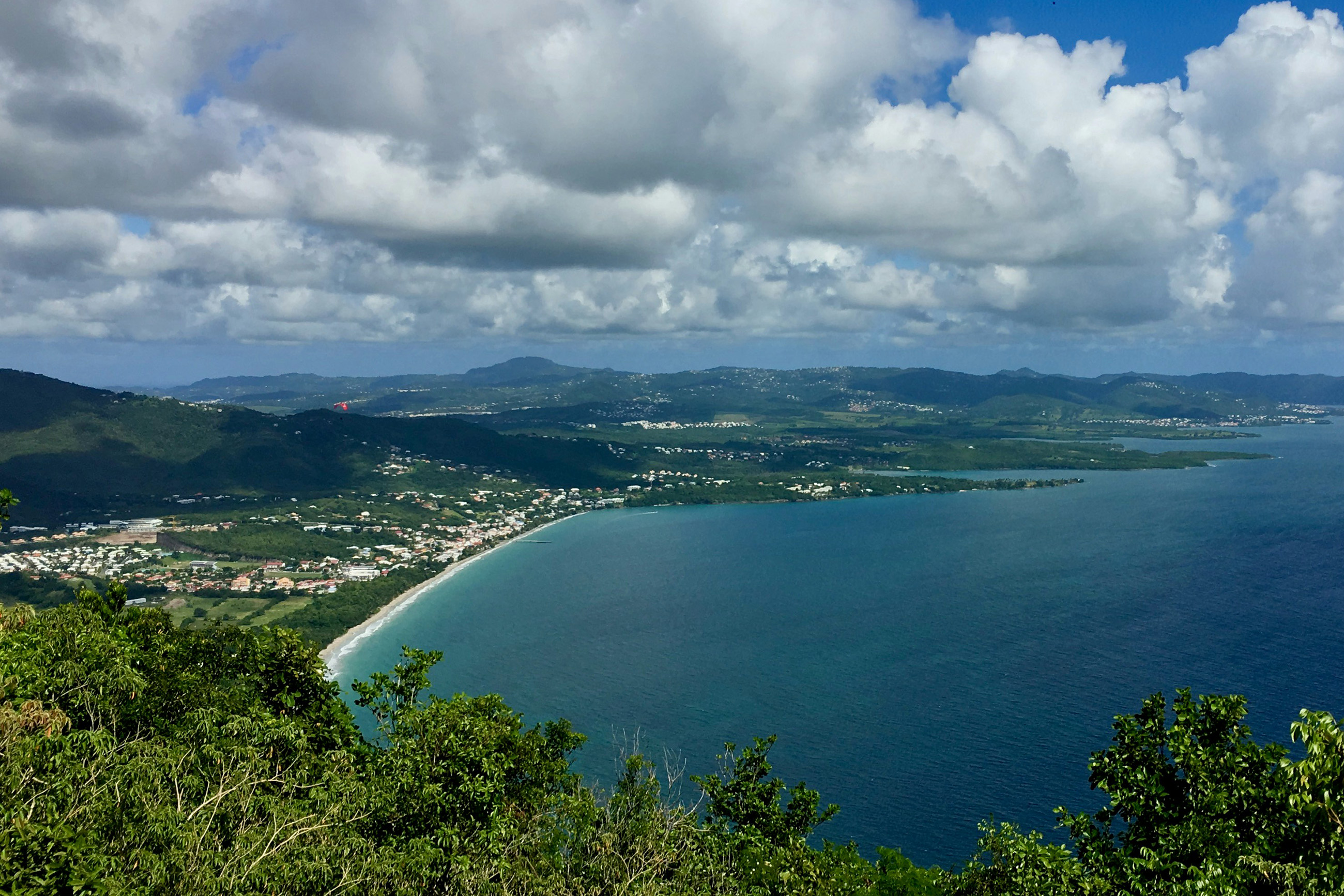 Aerial shot of a Caribbean tropical island with a sandy beach, a town, lush vegetation, and distant mountains.