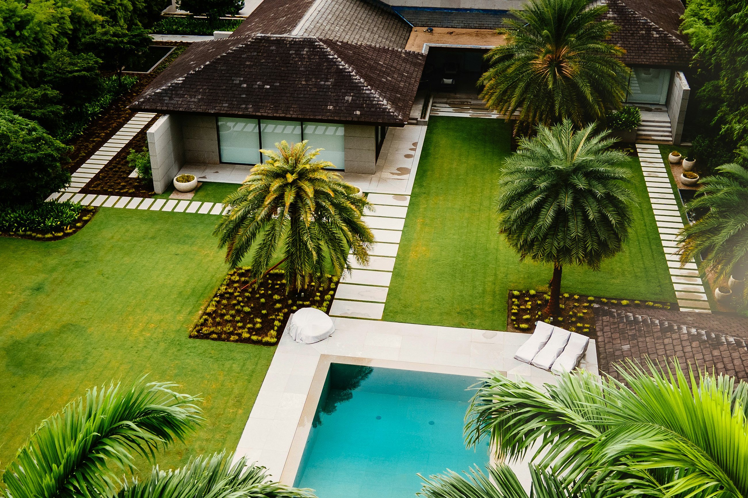 Aerial view of a Caribbean villa's backyard with a swimming pool, palm trees, and manicured gardens.