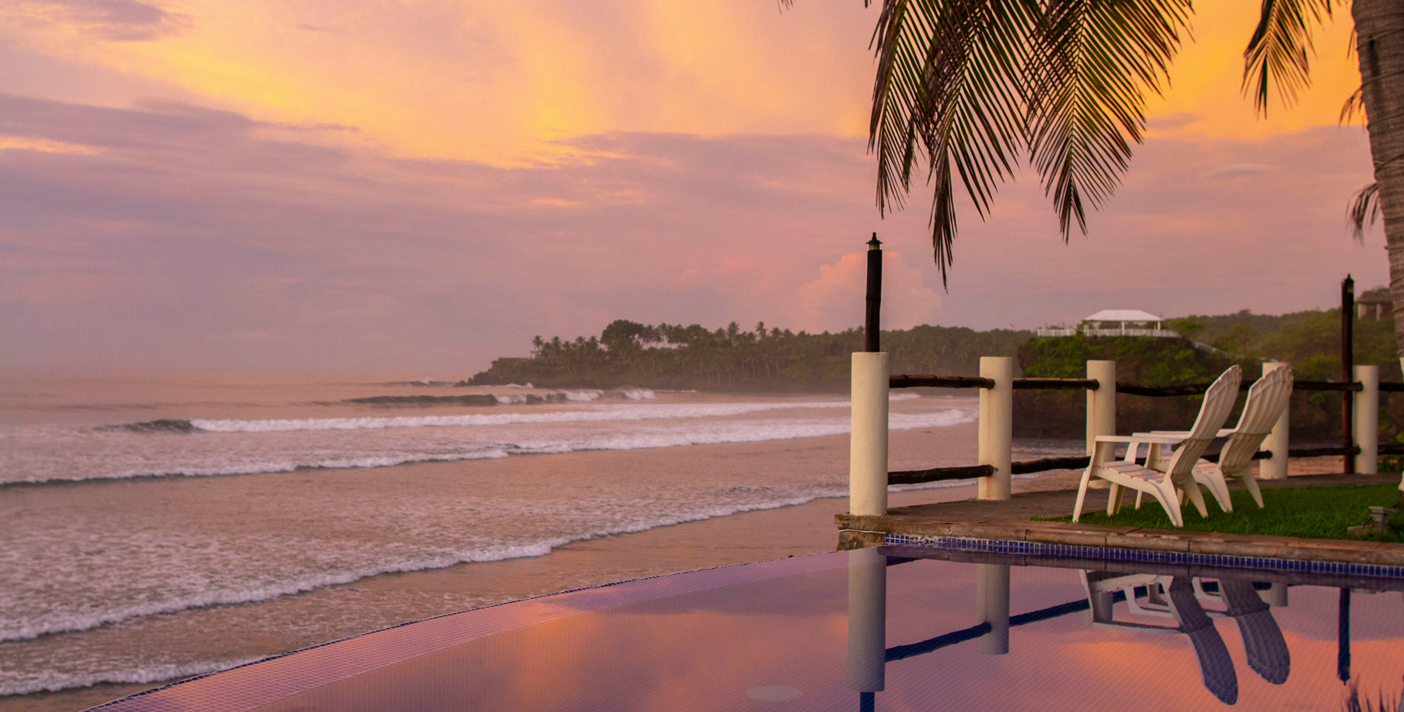 Two chairs facing the ocean at sunset with pink and yellow skies, where anyone would want to live in El Salvador.