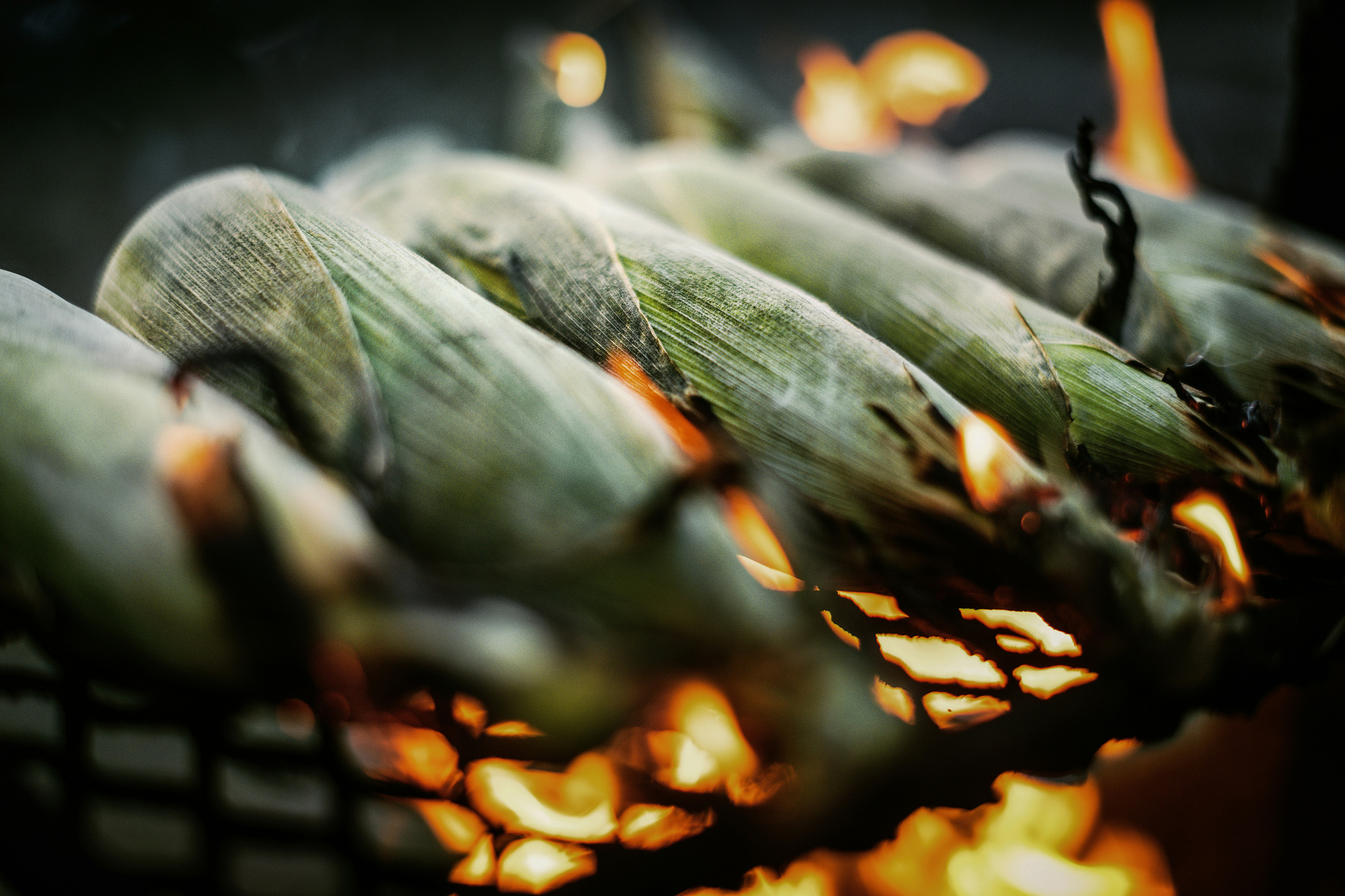 Grilled Mexican corn on the cob being prepared over an open flame.
