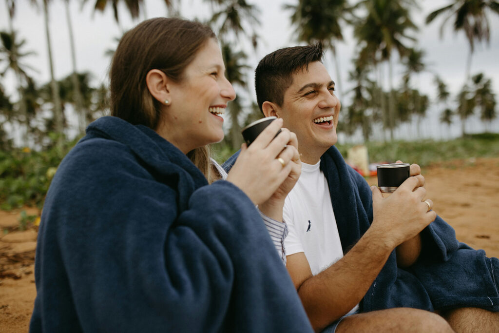 A couple sitting by the beach, smiling and drinking morning coffee enjoying their Independent Territory lifestyle.