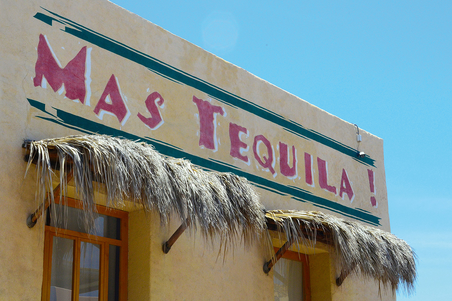 Rustic palm-thatched bar with Mas Tequila sign in a beach town in Mexico.