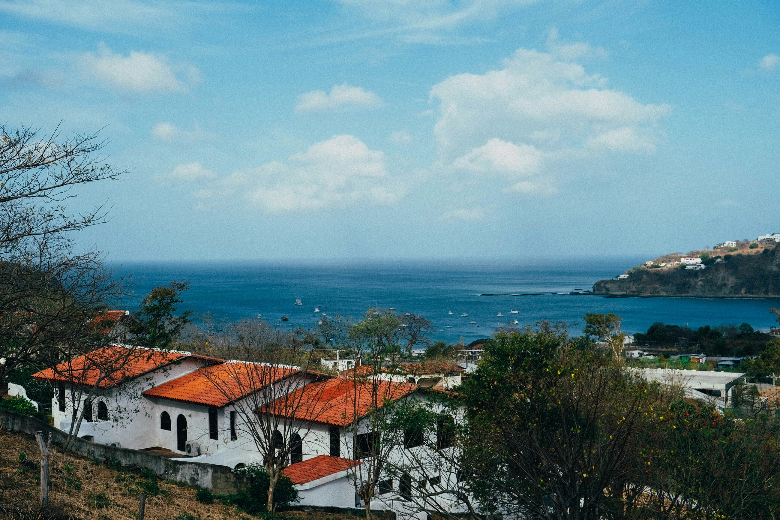 A view of red-tiled roof houses overlooking the bay of San Juan del Sur, with the scenic coastline and hills in the distance, highlighting the best areas to live in the region.