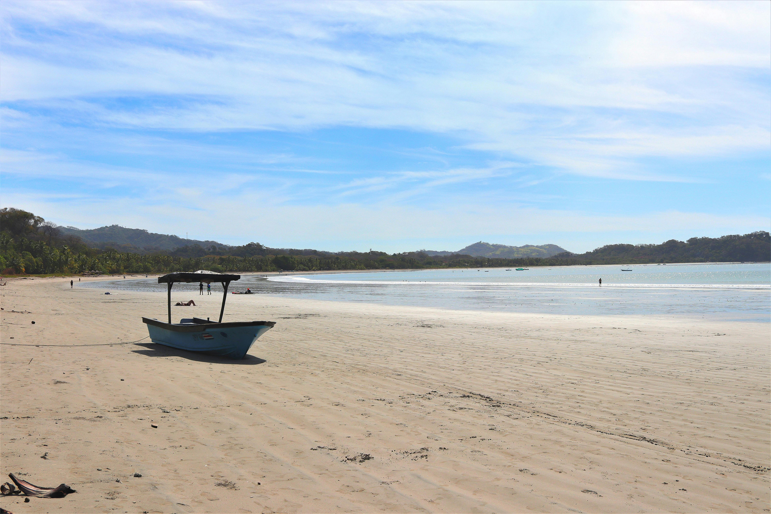 A boat sitting on a white sandy beach in Costa Rica with the tide out.