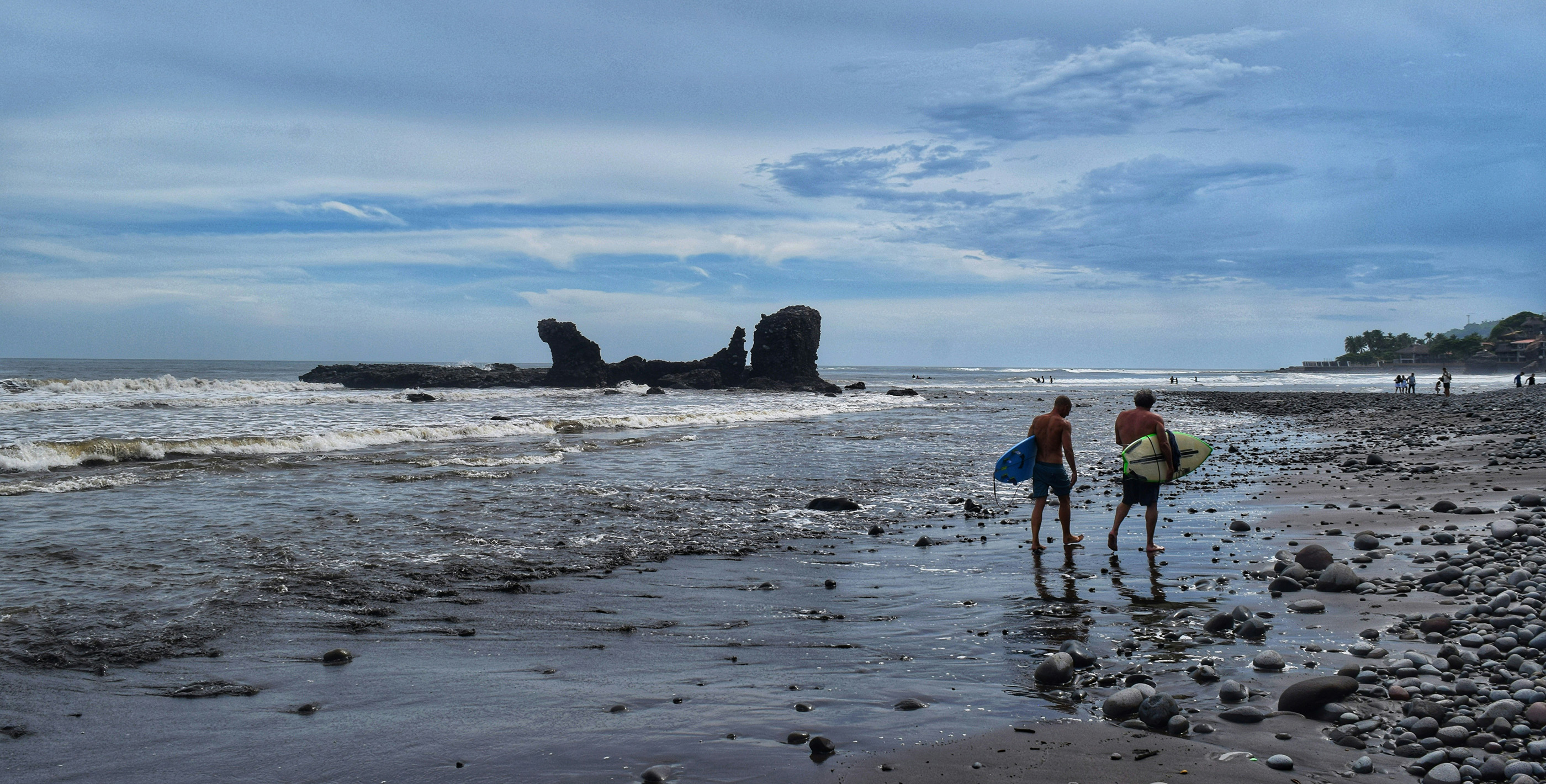 Surfers walking along a pebbled beach in El Salvador
