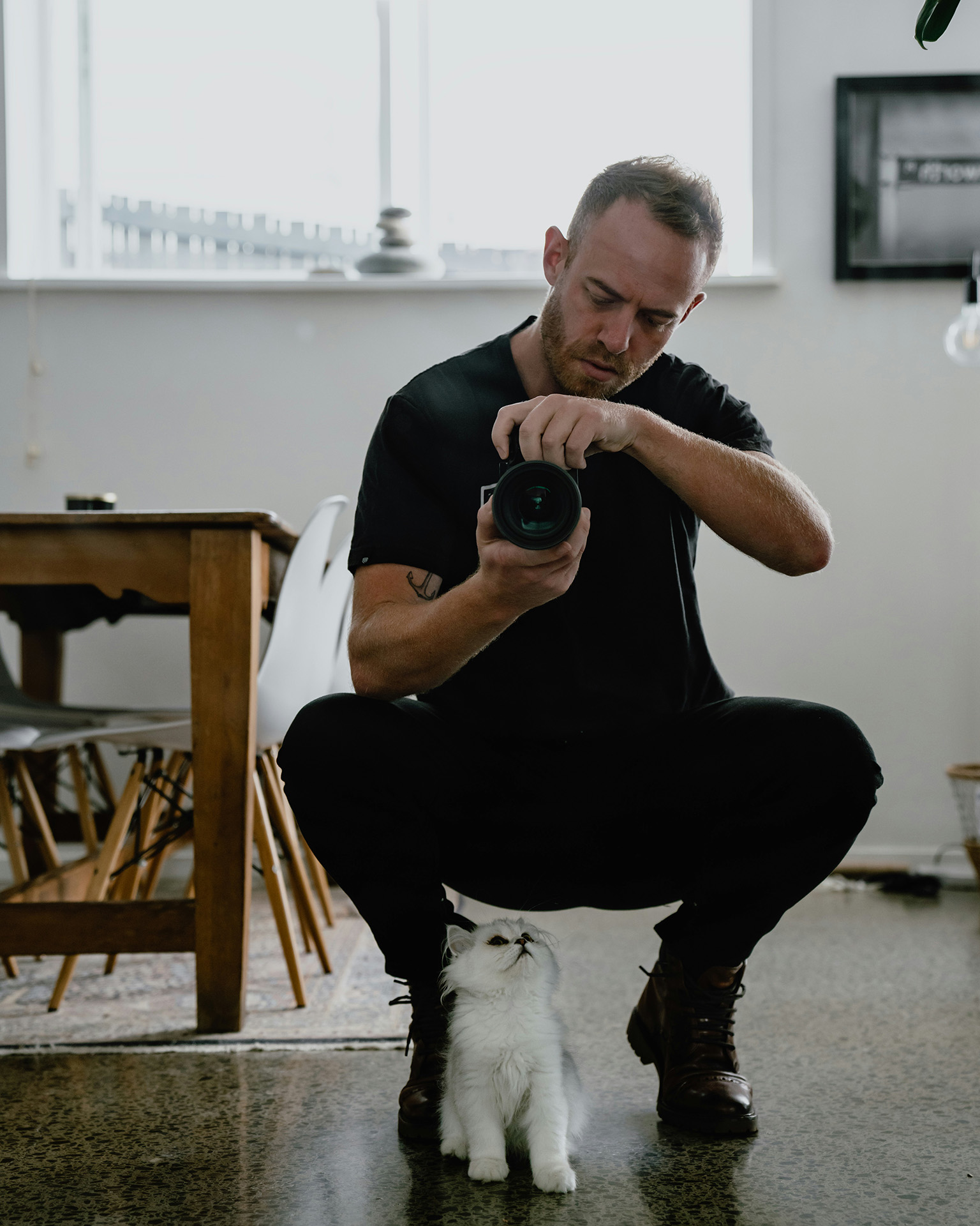 A man working remotely with a camera, while a cute baby cat looks up at him.
