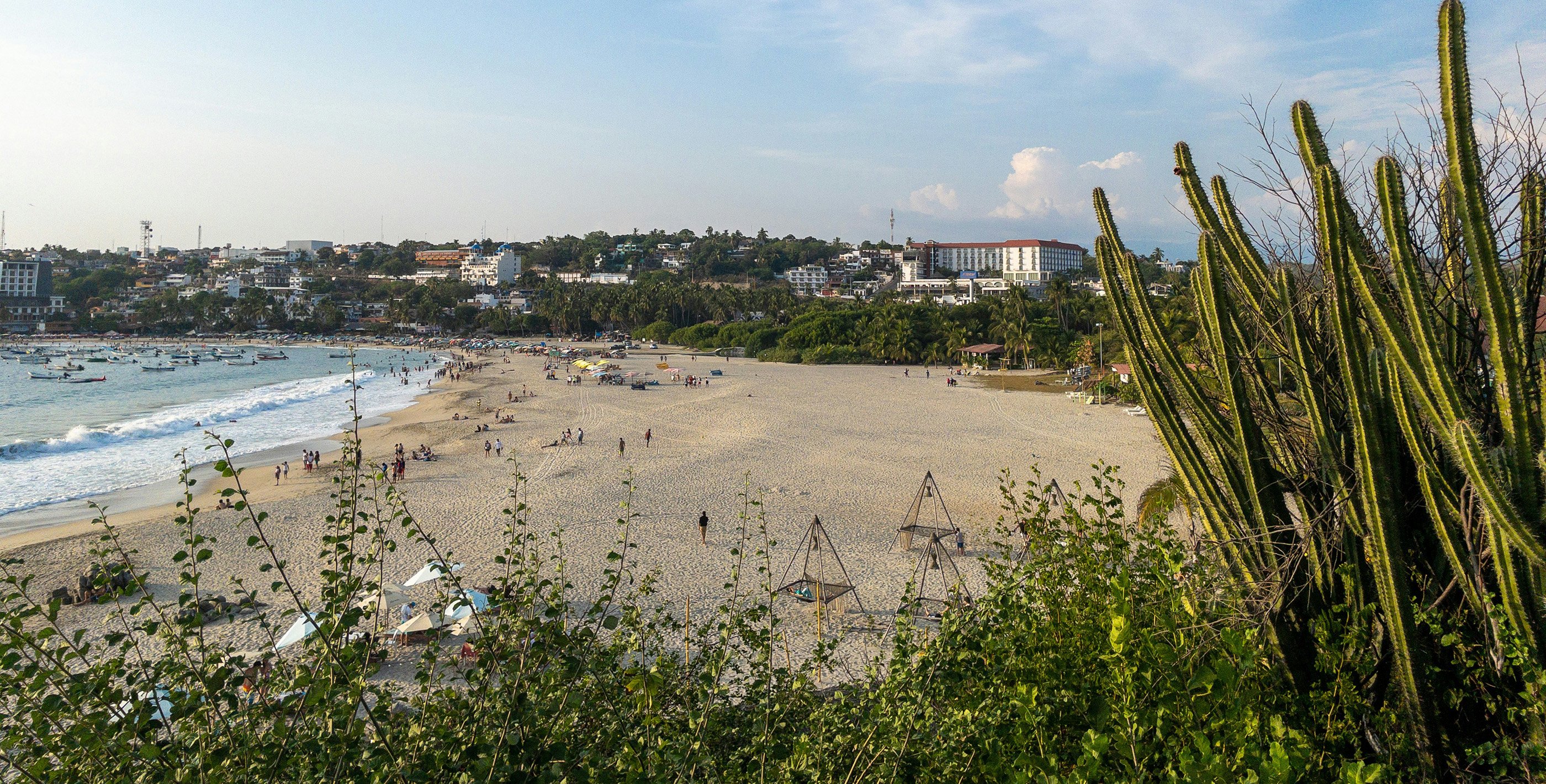 Busy beach in Puerto Escondido, Mexico, with locals and visitors enjoying the sun and ocean.