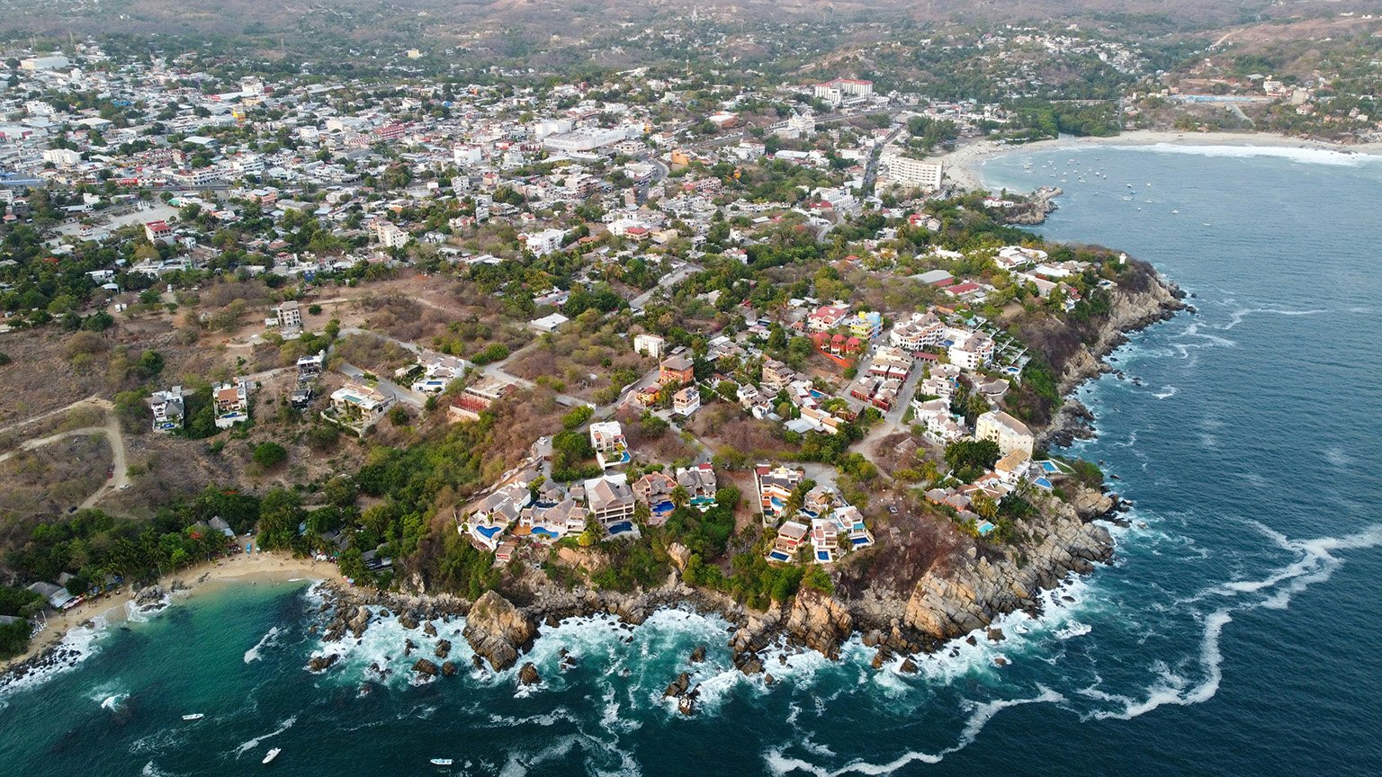Aerial shot of Puerto Escondido, Mexico, showing the rocky coastline and Playa Escondido in the background