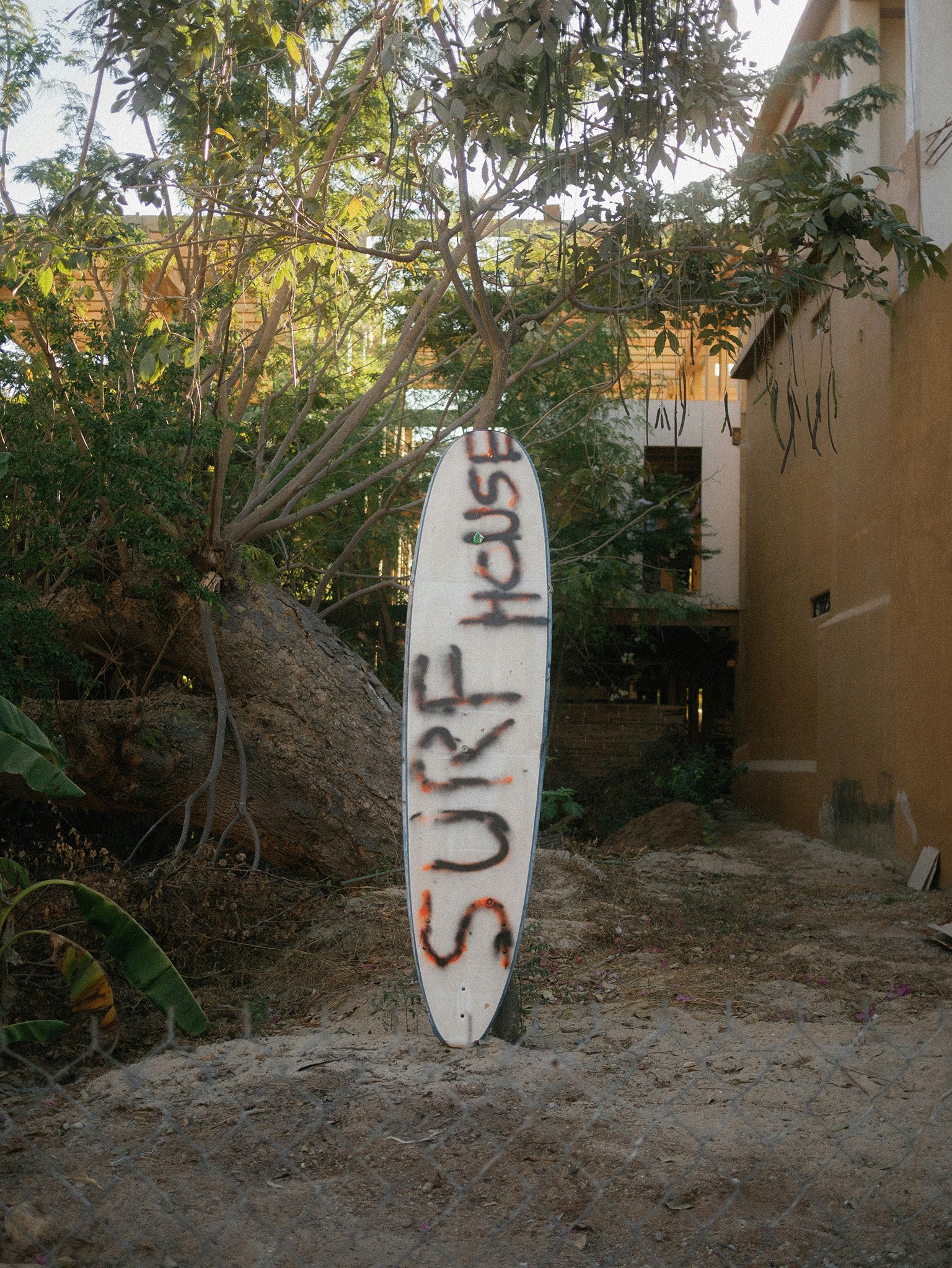A surfboard with "Surf House" printed on it stands upright in the sand, highlighting what living in Puerto Escondido can be