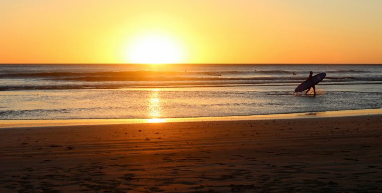 Surfer coming out of the water at sunset, showcasing the area's natural beauty and highlighting why it's a great place to live in San Juan del Sur.