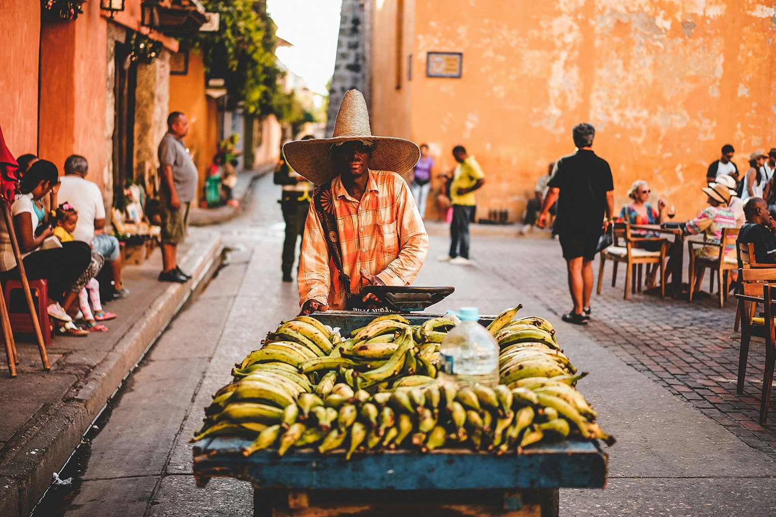 A Colombian man wearing a large hat, selling bananas from a wooden cart in Cartagena