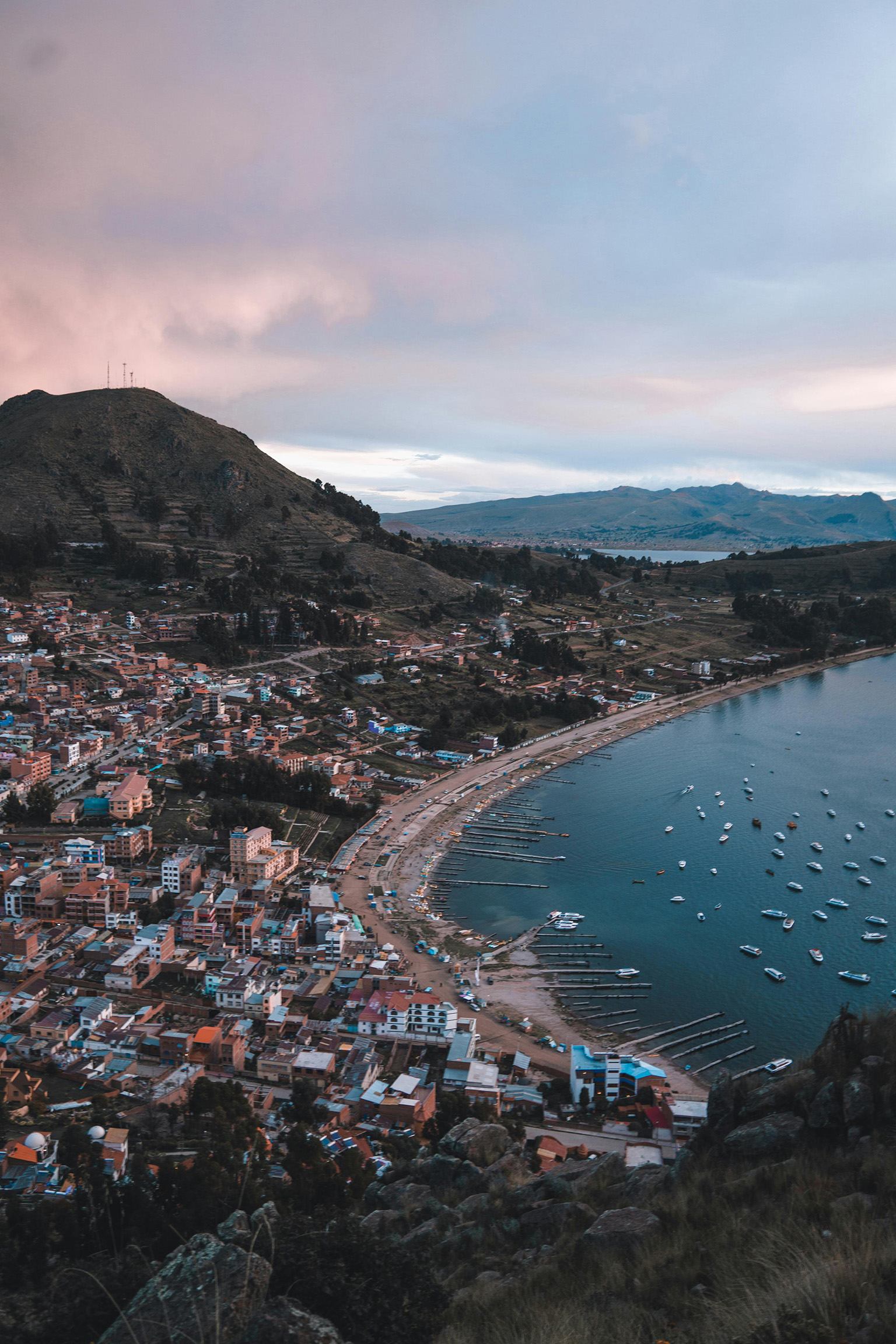 A scenic view of Copacabana, Bolivia, with boats in the bay and the vast landscape in the distance.