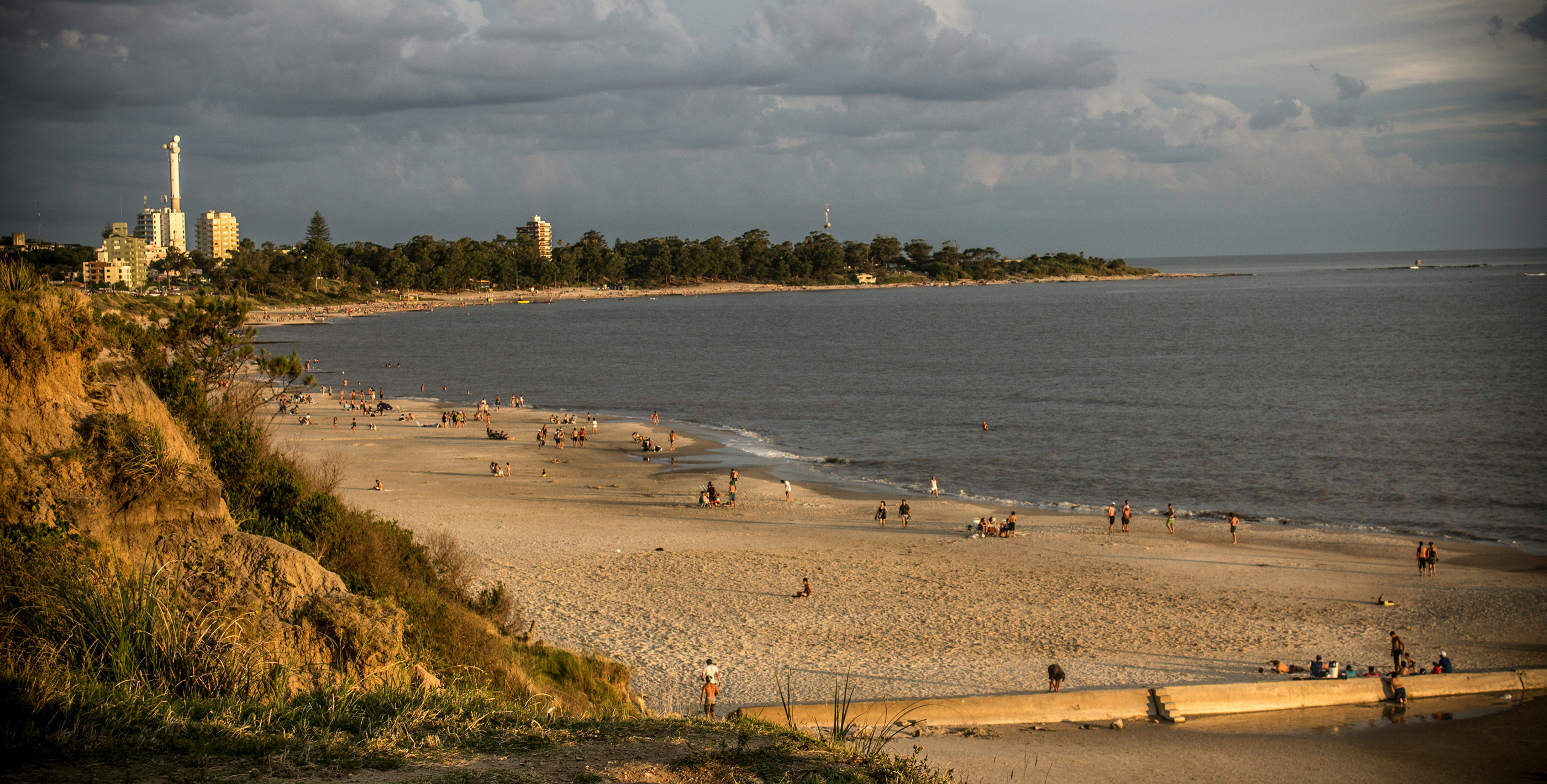 People living in Uruguay enjoying a sunset on a beach in Uruguay, with golden skies, calm waves and trees in the background
