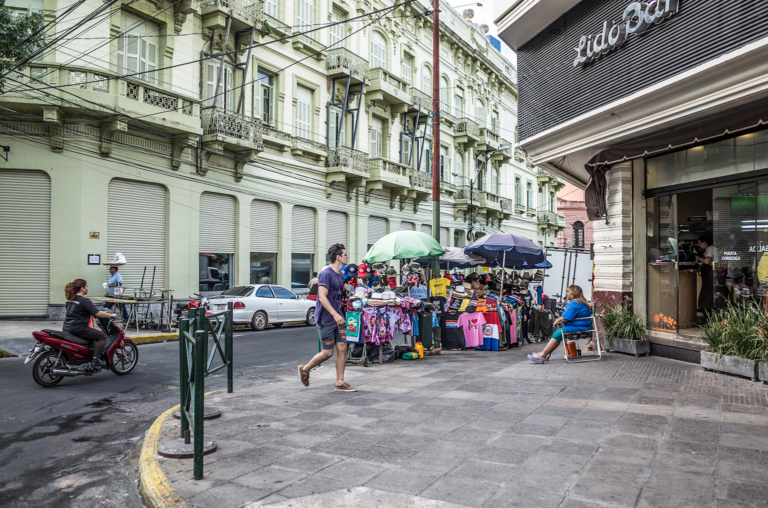 Downtown Asunción street corner with a man walking toward Lido Bar, street vendors, and colonial-style buildings