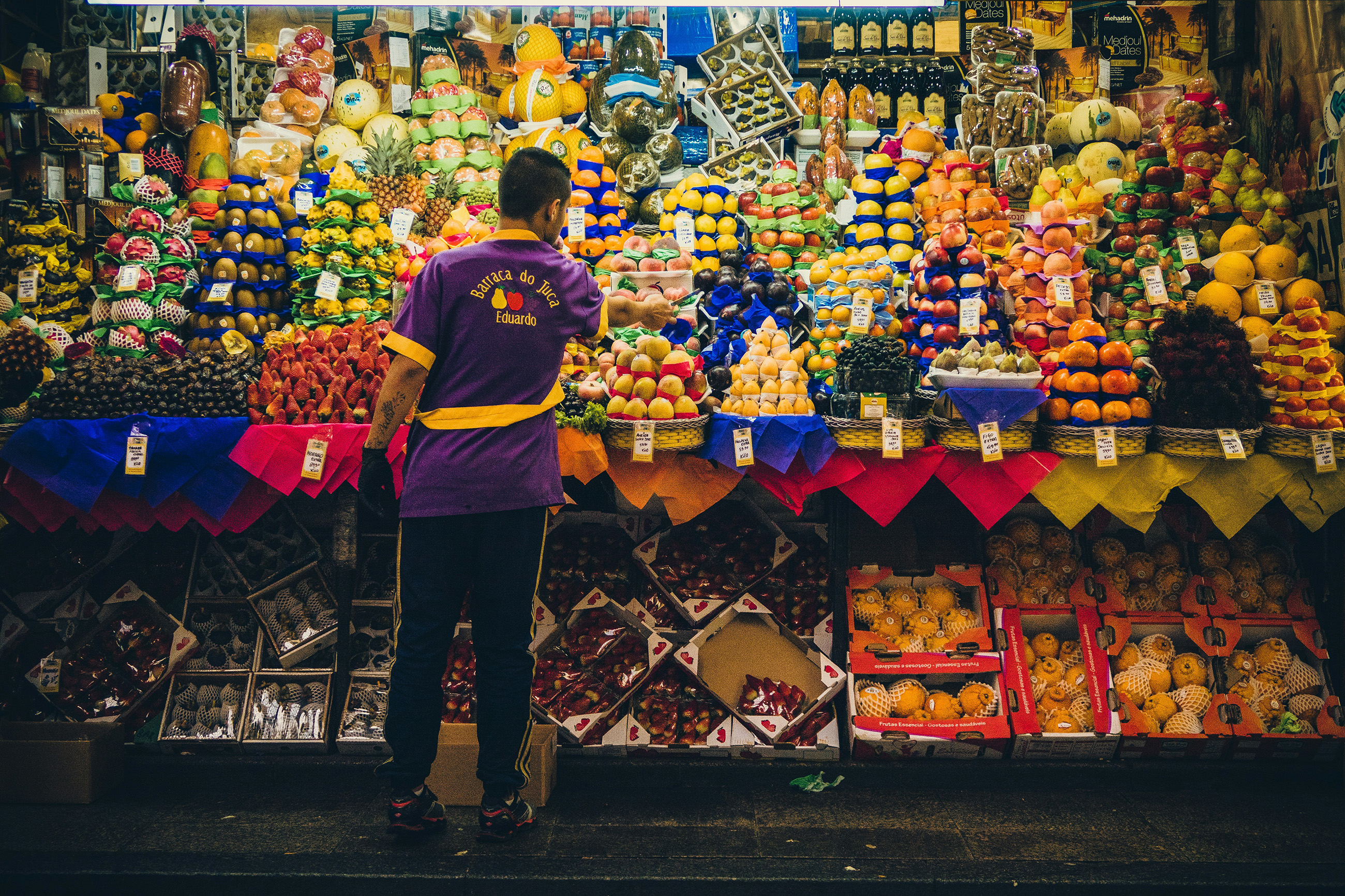 Vendor surrounded by fresh fruits and vegetables in Mercadão de São Paulo.