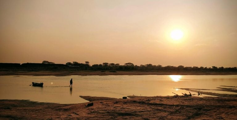 Daily life in Paraguay at sunset, showing a man pulling a wooden boat along a quiet river