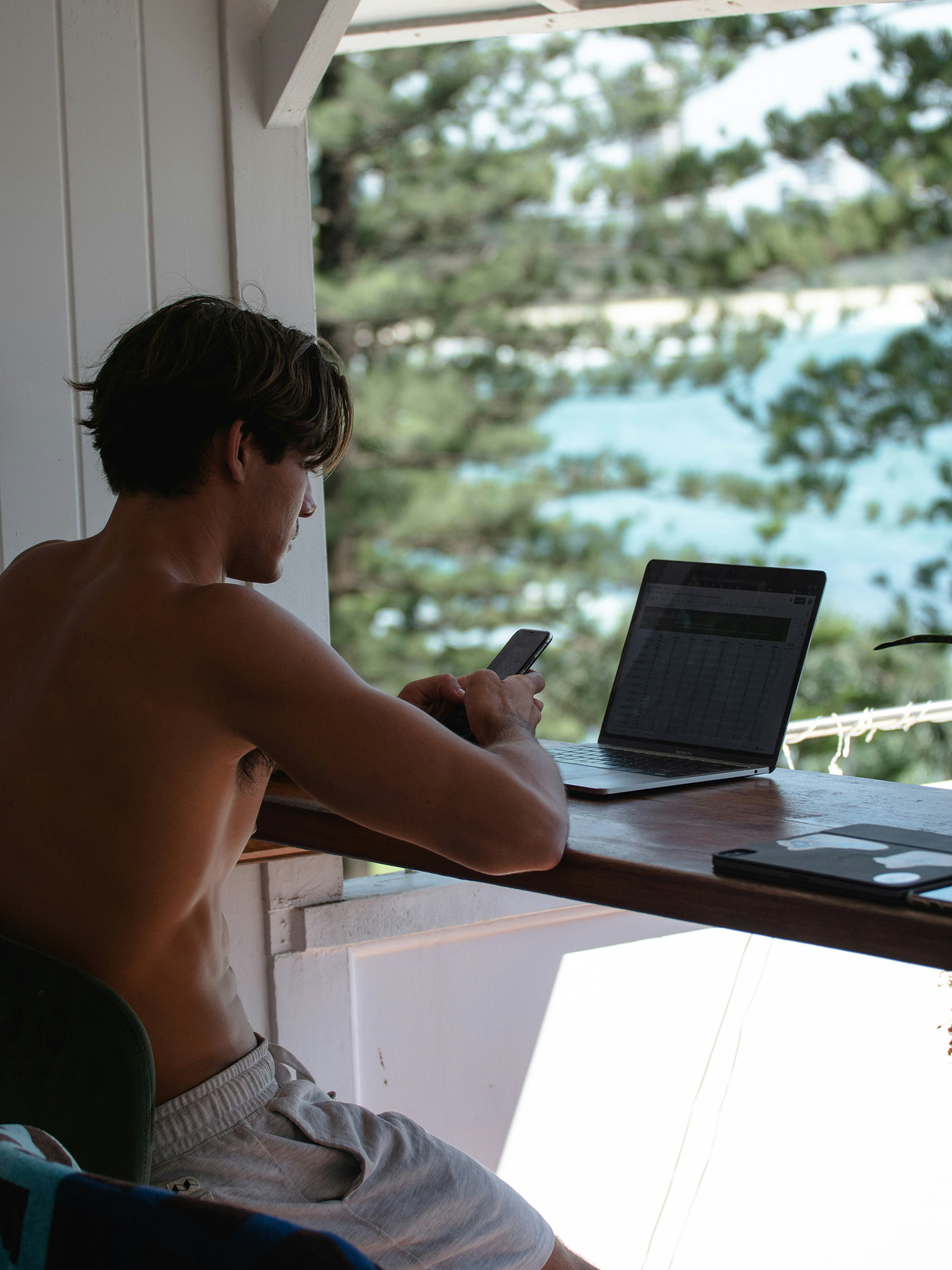 Remote worker in shorts using laptop and phone on his deck on the Corn Islands Nicaragua