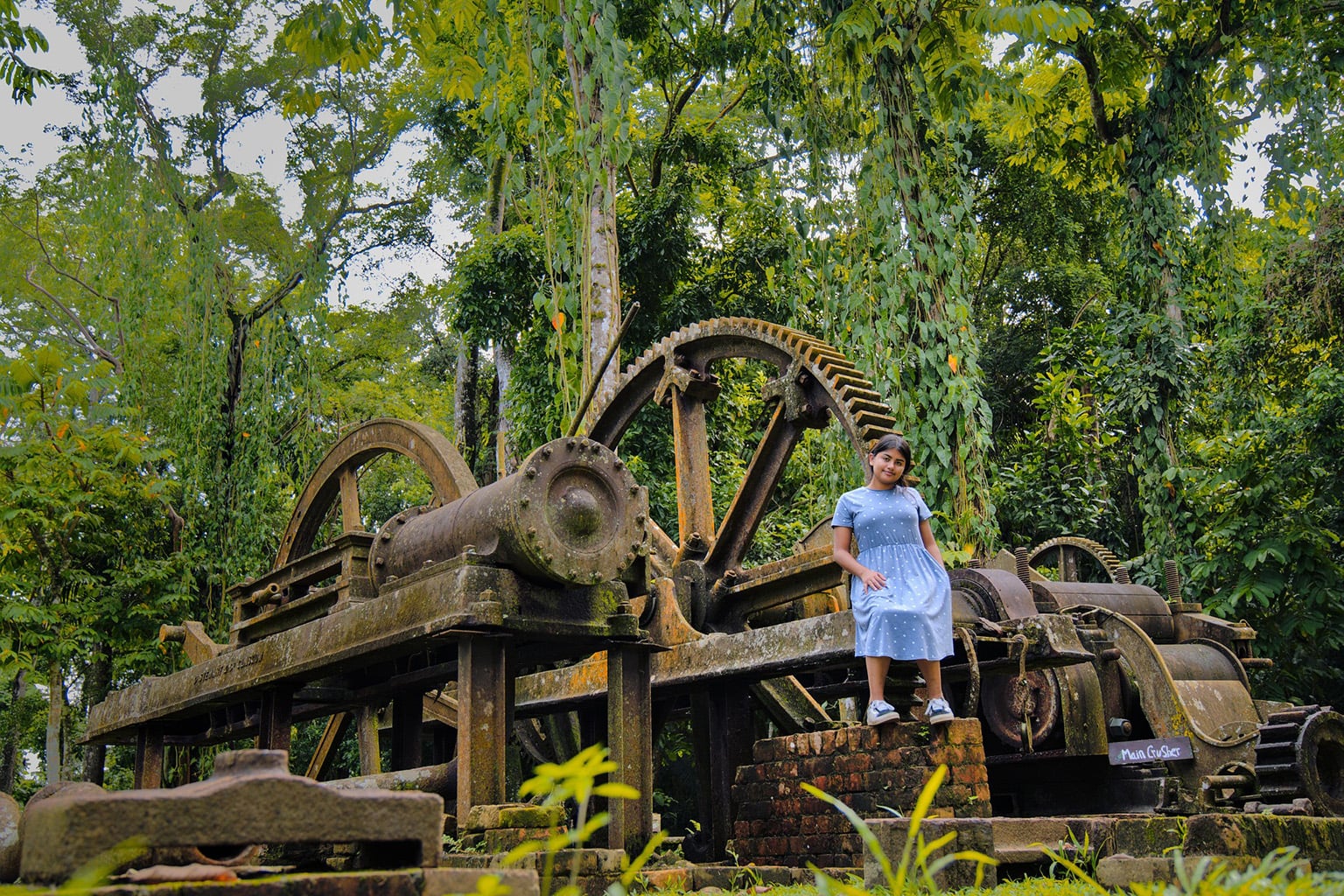 Living in Belize with a local girl standing near old sugar cane mill machinery