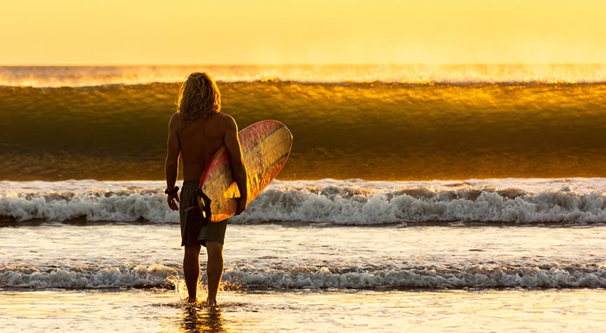 Expat with surfboard on Nicaragua beach at sunset