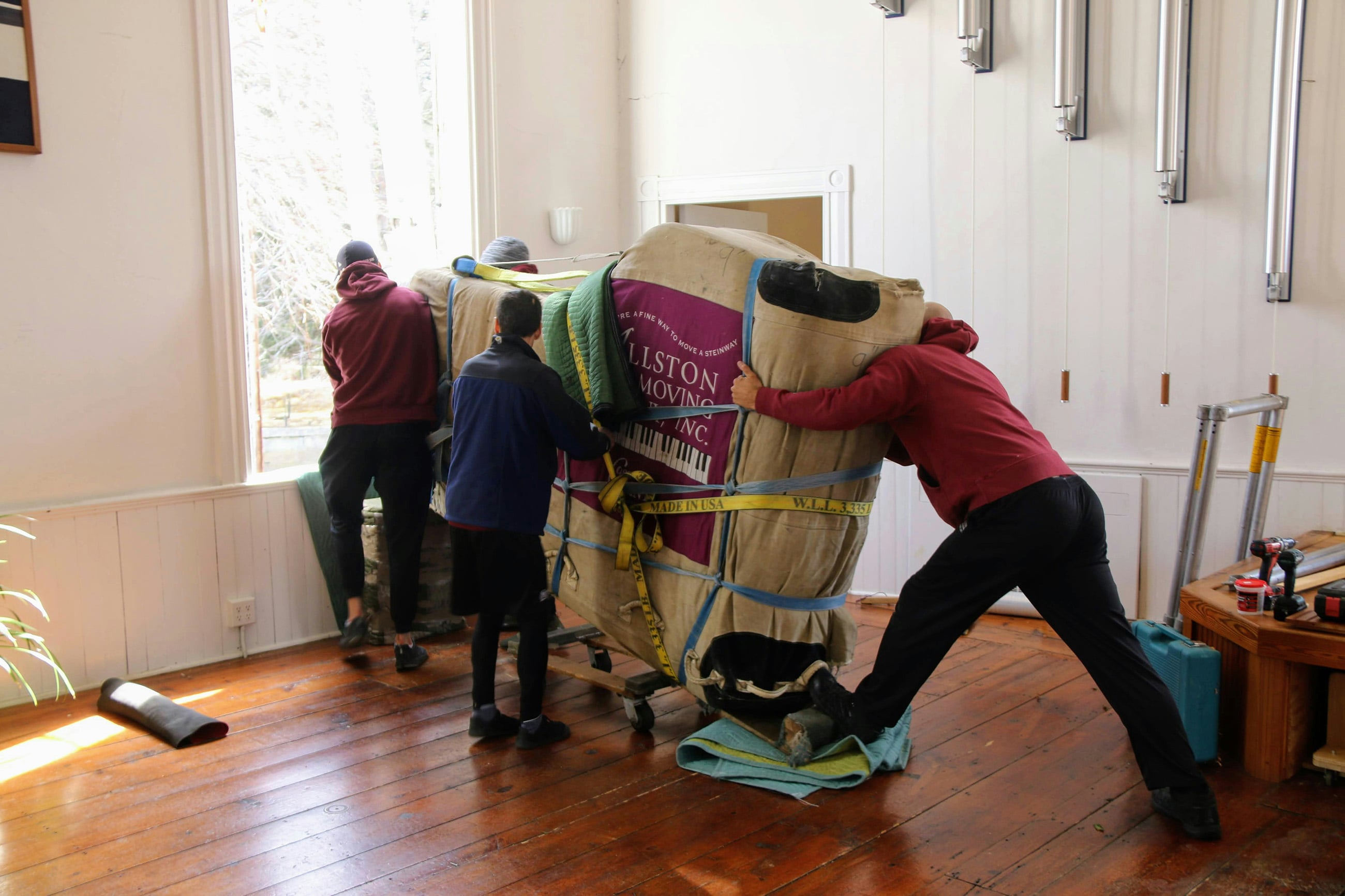 underinsuring-high-value-items-piano-move Moving crew carefully lifting a piano through a window, illustrating the risk of under insuring high-value items