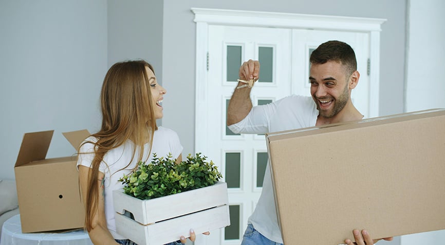 Couple moving boxes into their new home, man holding keys after buying property while living in Paraguay