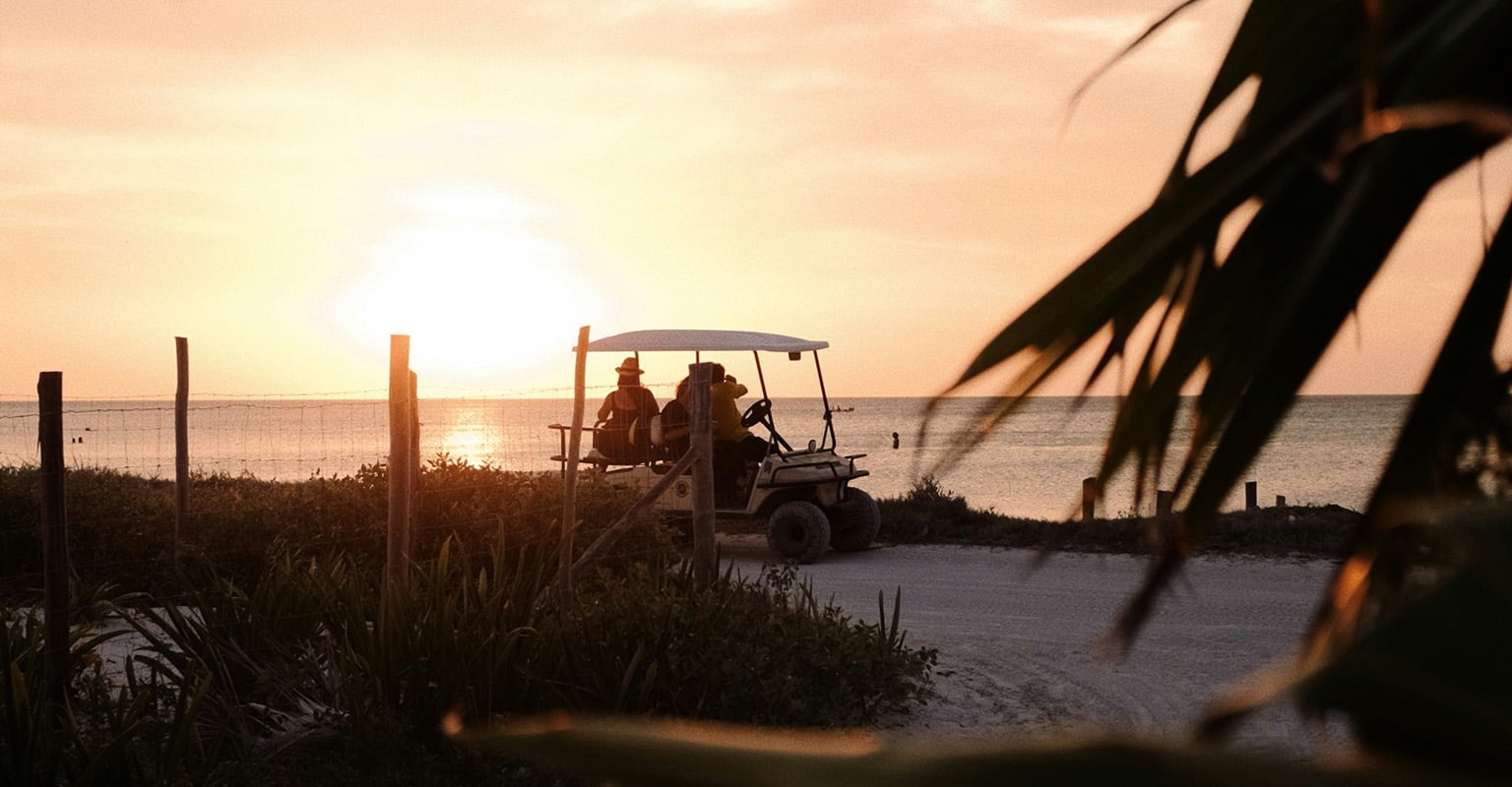 living-in-belize-golf-cart-beach-daily-life Couple in a golf cart along a tropical coastal road in Belize, illustrating everyday life in Belize