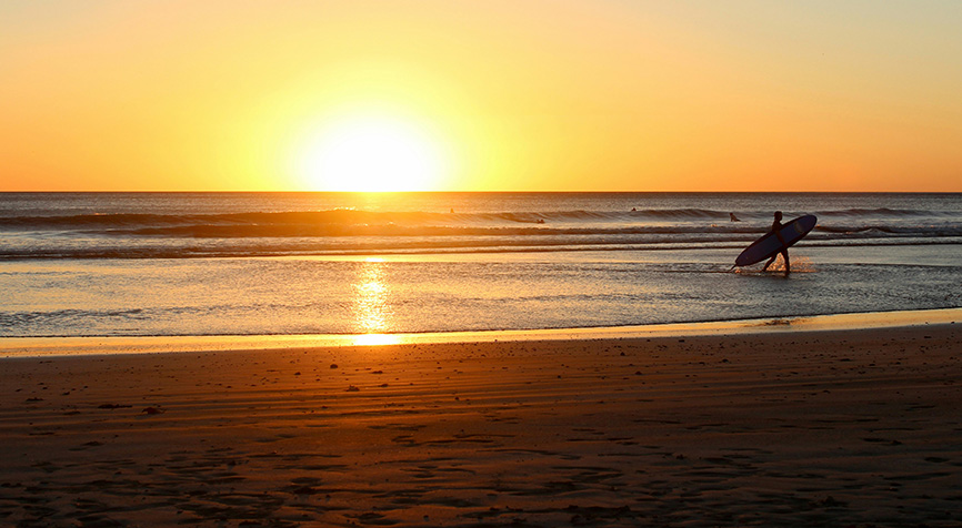 Surfer emerging from the water at sunset in San Juan del Sur, Nicaragua, highlighting living in Nicaragua.